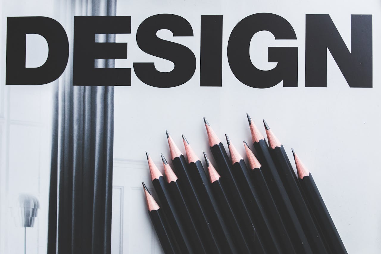 about-us-02 Black pencils arranged creatively next to large typography 'DESIGN'.